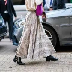 Elegancka długa spódnica w wężowy wzór, zestawiona z botkami i fioletową torebką, tworzy modne stylizacje.