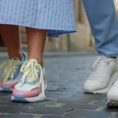 Kolorowe, modne sneakersy 2026 na nogach osoby w sukience i białe na nogach w jeansach, spacerujące po bruku.