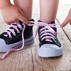 Dziecko uczy się, jak nauczyć dziecko wiązać buty, ćwicząc na czarnych trampkach z różowymi sznurówkami.