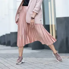 Kobieca stylizacja: pudrowa marynarka i plisowana spódnica. Jakie buty do plisowanej spódnicy? Sneakersy w tym samym kolorze tworzą modny look.