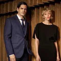 Elegancka para w stylizacjach cichy luksus. Mężczyzna w granatowym garniturze w prążki, kobieta w czarnej sukience.