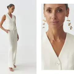 Elegancka kamizelka damska w kremowym kolorze, idealna do stylizacji z szerokimi spodniami. Długie, złote kolczyki dodają szyku.