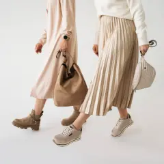 Dwie kobiety prezentują jesienne stylizacje. Jedna w beżowej sukience i botkach, druga w plisowanej spódnicy i sneakersach. Idealne buty na jesień.