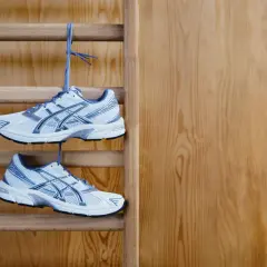 Białe buty sportowe z niebieskimi detalami wiszą na drabince gimnastycznej. Idealne buty na WF, gotowe do treningu.
