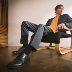 Mężczyzna w granatowej marynarce i musztardowym swetrze, spodnie i eleganckie buty tworzą stylowy ubiór casual.