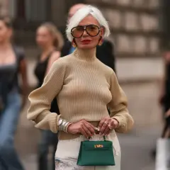 Elegancka kobieta prezentuje stylowe stylizacje dla dojrzałych pań. Beżowy golf, wzorzysta spódnica i zielona torebka tworzą szykowny look.