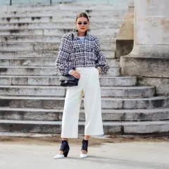 Elegancka kobieta w białych kulotach i tweedowej marynarce, z czarną torebką na ramieniu. Stylowe kuloty stylizacje.