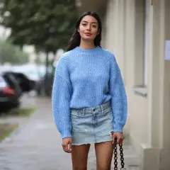 Niebieski sweter i jeansowa spódnica to idealne połączenie. Modelka prezentuje, jaka bluzka do jeansowej spódnicy pasuje najlepiej.