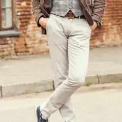 Elegancki mężczyzna w jasnych spodniach i kamizelce, z rękami w kieszeniach. Idealne buty do jasnych spodni to ciemne sneakersy.
