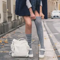 Stylizacja z długimi skarpetkami damskimi: szare, prążkowane, sięgające do połowy uda, zestawione z białą torebką i płaskimi butami.