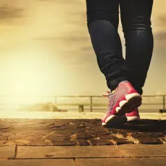 Kobieta w dżinsach i różowych butach sportowych idzie po kamiennej nawierzchni. Czy buty na styk, czy większe?