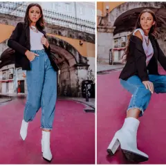 Kobieta w modnych mom jeans stylizacjach, czarnej marynarce i białych kozaczkach na różowym tle.