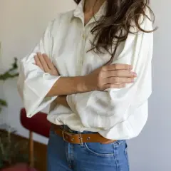 Kobieta w białej koszuli oversize i jeansach, z paskiem. Pokazuje, jak nosić koszulę oversize, tworząc luźny, ale stylowy look.