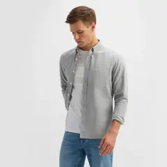 Młody mężczyzna w eleganckim ubiorze męskim: szara koszula z długim rękawem, biały t-shirt i jeansy.