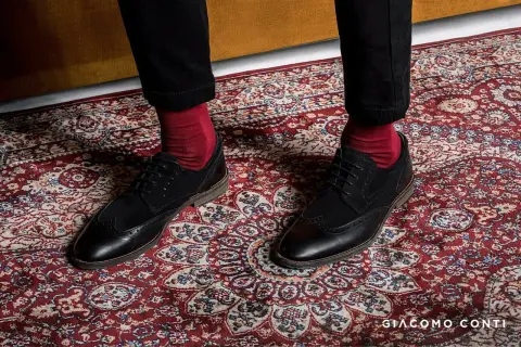 Czerwone skarpety do garnituru? Tak! Eleganckie czarne buty i bordowy dywan tworzą stylowy zestaw.