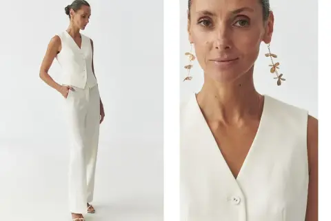 Elegancka kamizelka damska w kremowym kolorze, idealna do stylizacji z szerokimi spodniami. Długie, złote kolczyki dodają szyku.