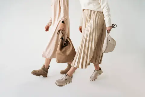 Dwie kobiety prezentują jesienne stylizacje. Jedna w beżowej sukience i botkach, druga w plisowanej spódnicy i sneakersach. Idealne buty na jesień.