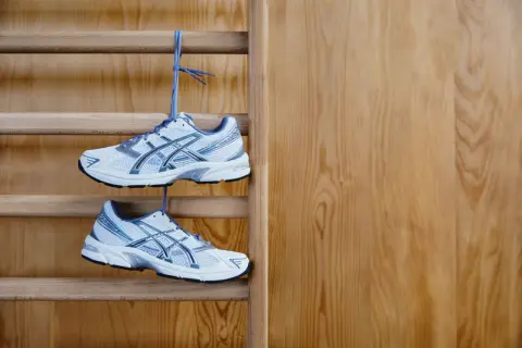 Białe buty sportowe z niebieskimi detalami wiszą na drabince gimnastycznej. Idealne buty na WF, gotowe do treningu.