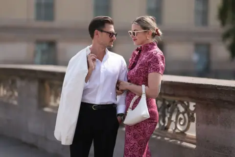 Elegancka para, inspiracja, jak się ubrać na poprawiny. Ona w różowej sukience w róże, on w białej koszuli i czarnych spodniach.
