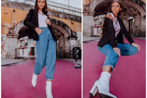 Kobieta w modnych mom jeans stylizacjach, czarnej marynarce i białych kozaczkach na różowym tle.