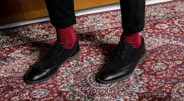 Czerwone skarpety do garnituru? Tak! Eleganckie czarne buty i bordowy dywan tworzą stylowy zestaw.