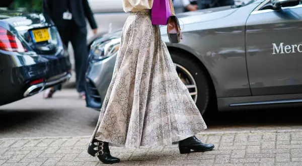 Elegancka długa spódnica w wężowy wzór, zestawiona z botkami i fioletową torebką, tworzy modne stylizacje.