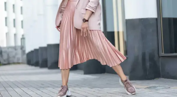Kobieca stylizacja: pudrowa marynarka i plisowana spódnica. Jakie buty do plisowanej spódnicy? Sneakersy w tym samym kolorze tworzą modny look.