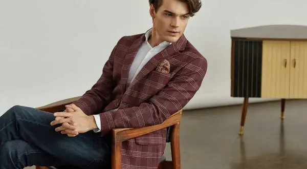 Elegancka marynarka męska do dżinsów w kratę, w odcieniu bordo. Model siedzi na drewnianym krześle, prezentując stylową stylizację.