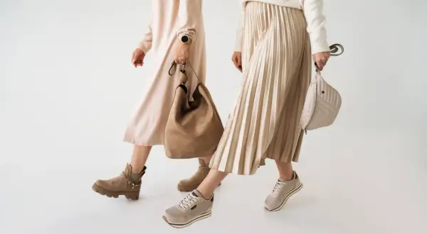 Dwie kobiety prezentują jesienne stylizacje. Jedna w beżowej sukience i botkach, druga w plisowanej spódnicy i sneakersach. Idealne buty na jesień.