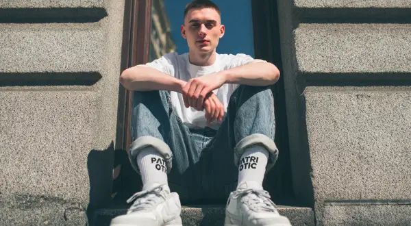 Młody mężczyzna w jeansach i białej koszulce prezentuje modne **wysokie skarpetki stylizacje**.
