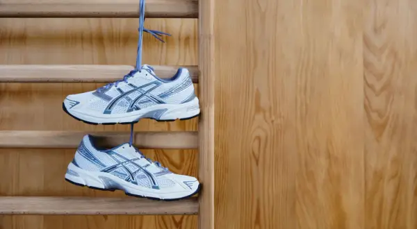 Białe buty sportowe z niebieskimi detalami wiszą na drabince gimnastycznej. Idealne buty na WF, gotowe do treningu.