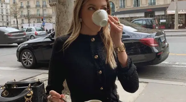 Elegancka kobieta w stylu "old money ubrania" pije kawę w paryskiej kawiarni.