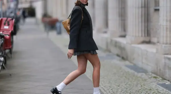 Dziewczyna w stylu coquette, w szarej beretce i krótkiej spódniczce, idzie ulicą.