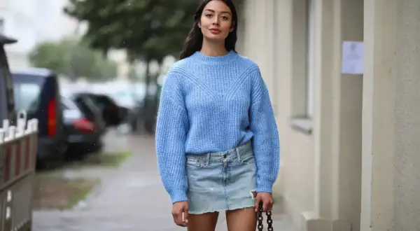 Niebieski sweter i jeansowa spódnica to idealne połączenie. Modelka prezentuje, jaka bluzka do jeansowej spódnicy pasuje najlepiej.