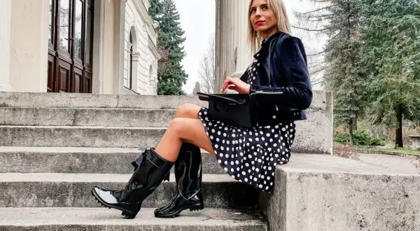 Elegancka kobieta w grochy, w czarnych, błyszczących kaloszach ze skarpetą, siedzi na kamiennych schodach.