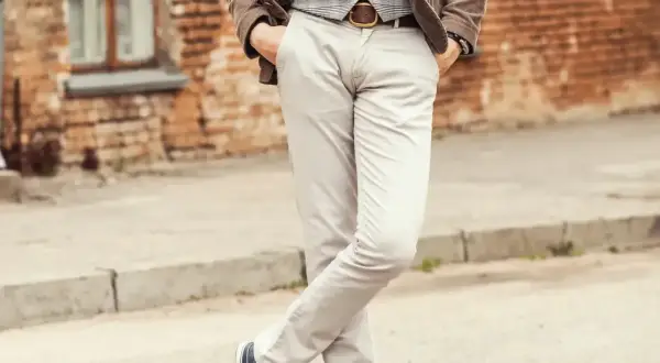 Elegancki mężczyzna w jasnych spodniach i kamizelce, z rękami w kieszeniach. Idealne buty do jasnych spodni to ciemne sneakersy.