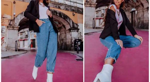 Kobieta w modnych mom jeans stylizacjach, czarnej marynarce i białych kozaczkach na różowym tle.