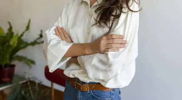 Kobieta w białej koszuli oversize i jeansach, z paskiem. Pokazuje, jak nosić koszulę oversize, tworząc luźny, ale stylowy look.
