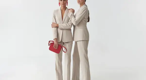 Dwie kobiety w beżowych, dopasowanych garniturach. Jedna trzyma czerwoną torebkę. To idealny **matching co to** za styl!