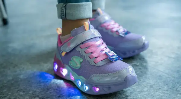 Fioletowe buty dziecięce z brokatem i różowymi sznurówkami. Ich podeszwa świeci kolorowymi serduszkami, tworząc magiczny efekt.
