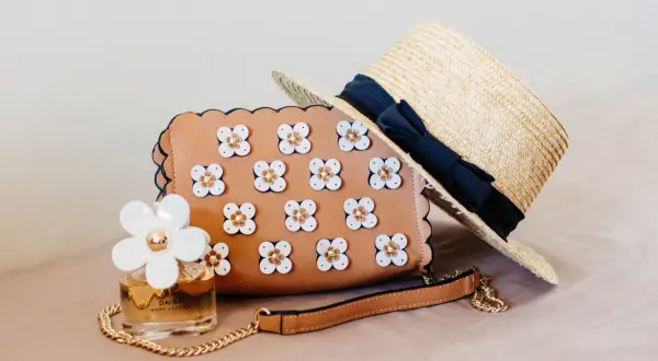 Brązowa torebka z kwiatkami, słomkowy kapelusz i perfumy Daisy. Idealny zestaw na letnie dni.