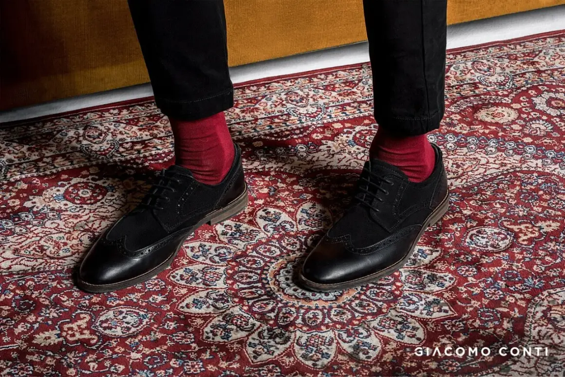 Czerwone skarpety do garnituru? Tak! Eleganckie czarne buty i bordowy dywan tworzą stylowy zestaw.
