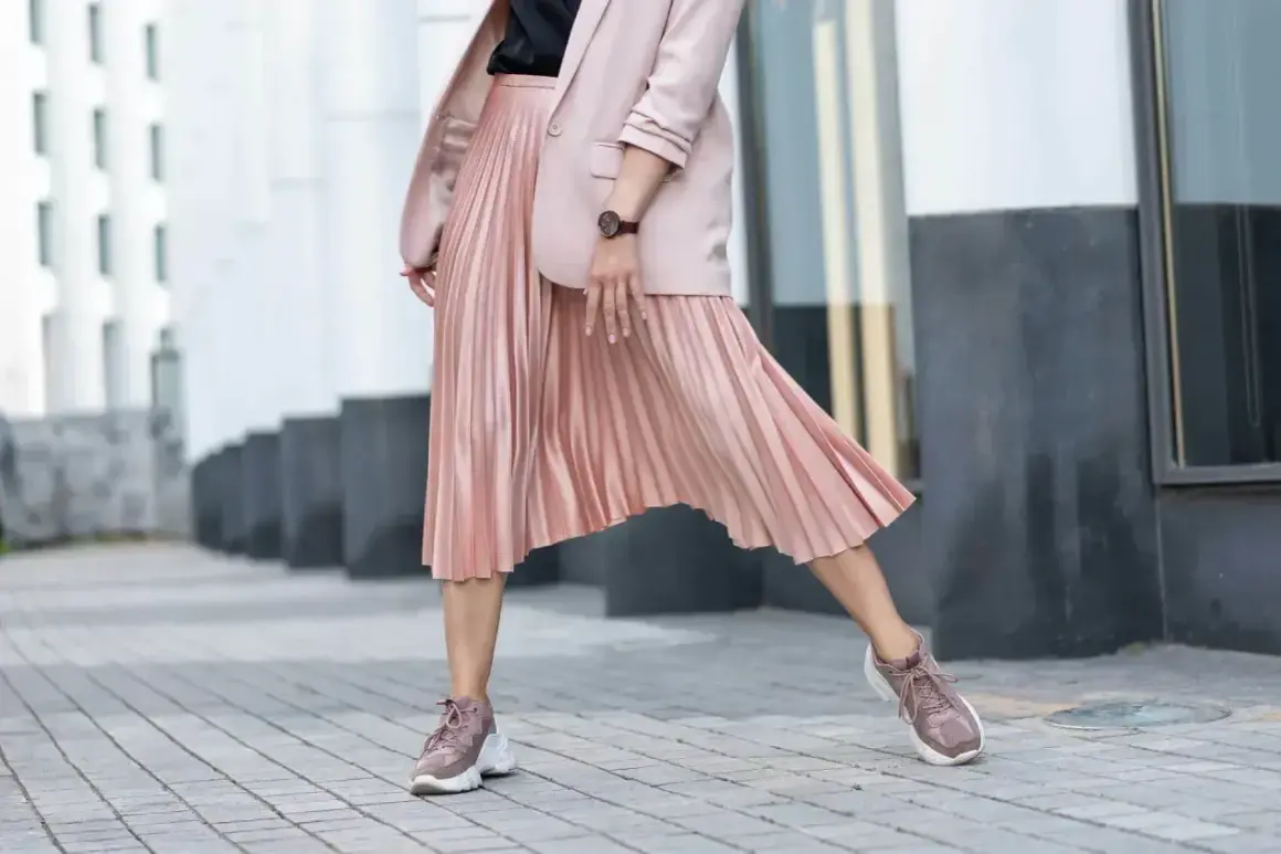 Kobieca stylizacja: pudrowa marynarka i plisowana spódnica. Jakie buty do plisowanej spódnicy? Sneakersy w tym samym kolorze tworzą modny look.