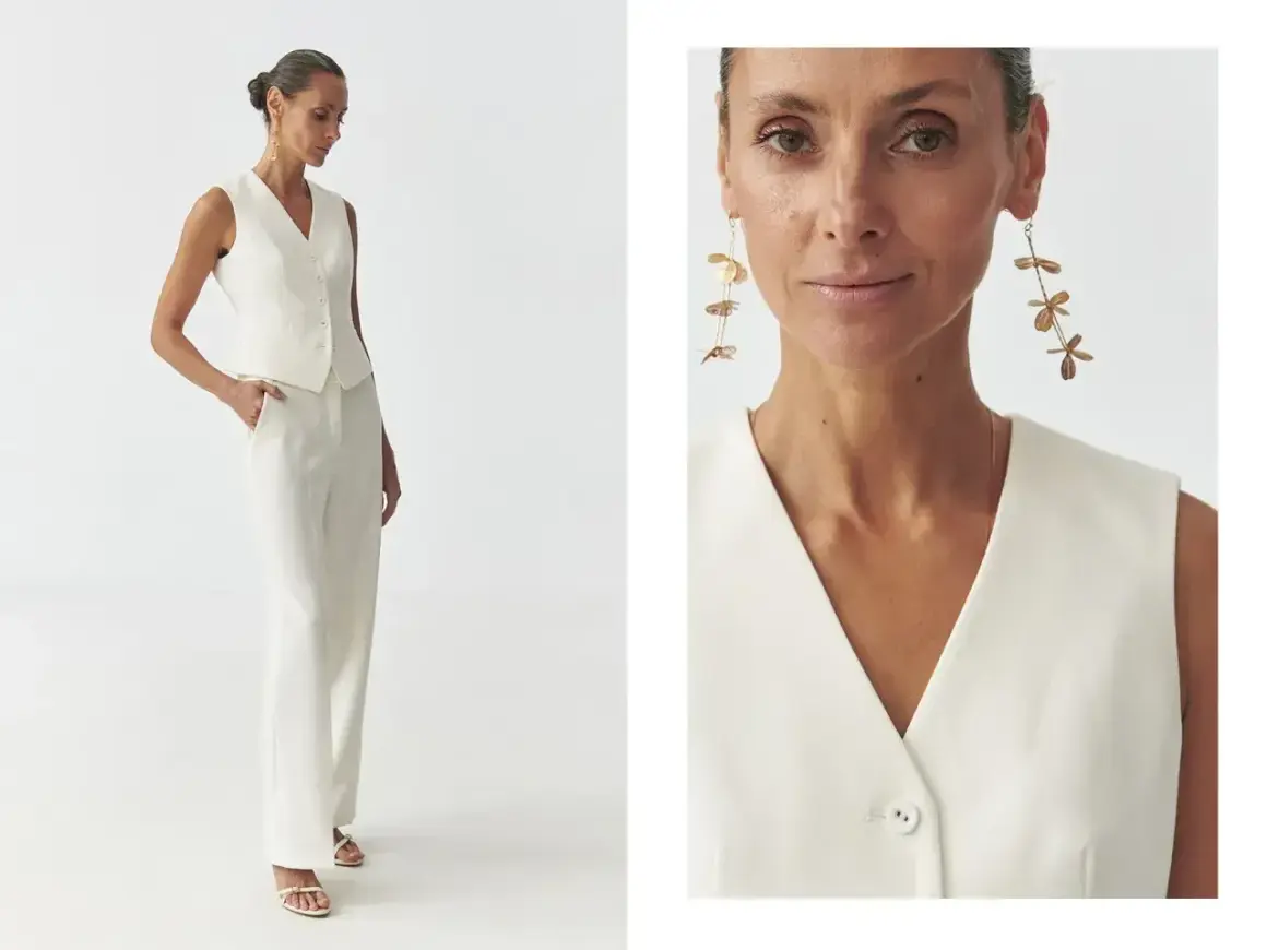 Elegancka kamizelka damska w kremowym kolorze, idealna do stylizacji z szerokimi spodniami. Długie, złote kolczyki dodają szyku.