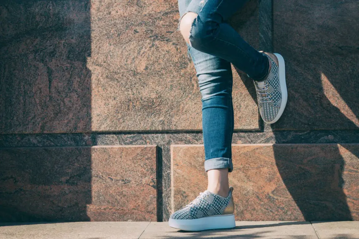 Nogawki jeansów podwinięte na kostkach, odsłaniające modne sneakersy. Idealny sposób, jak podwinąć spodnie na lato.
