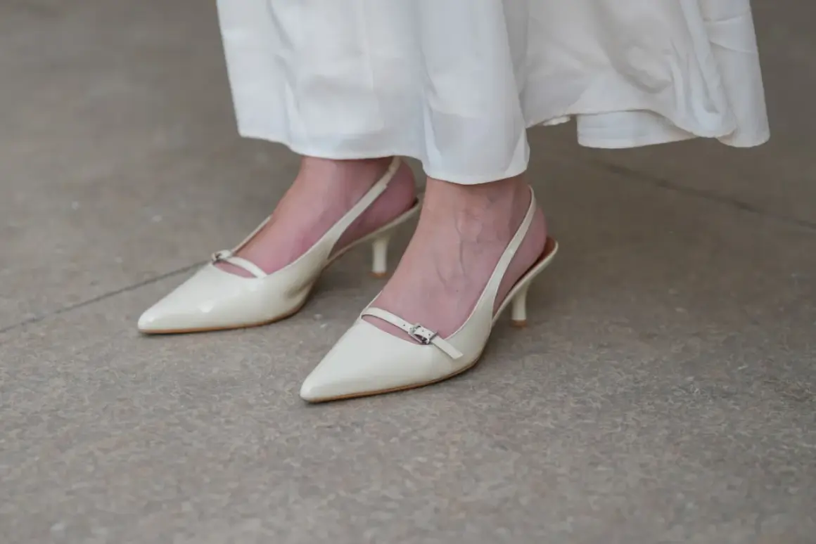Eleganckie, kremowe stopy w szpilkach z paskiem wokół kostki, idealne do letniej sukienki.