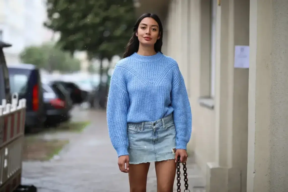 Niebieski sweter i jeansowa spódnica to idealne połączenie. Modelka prezentuje, jaka bluzka do jeansowej spódnicy pasuje najlepiej.