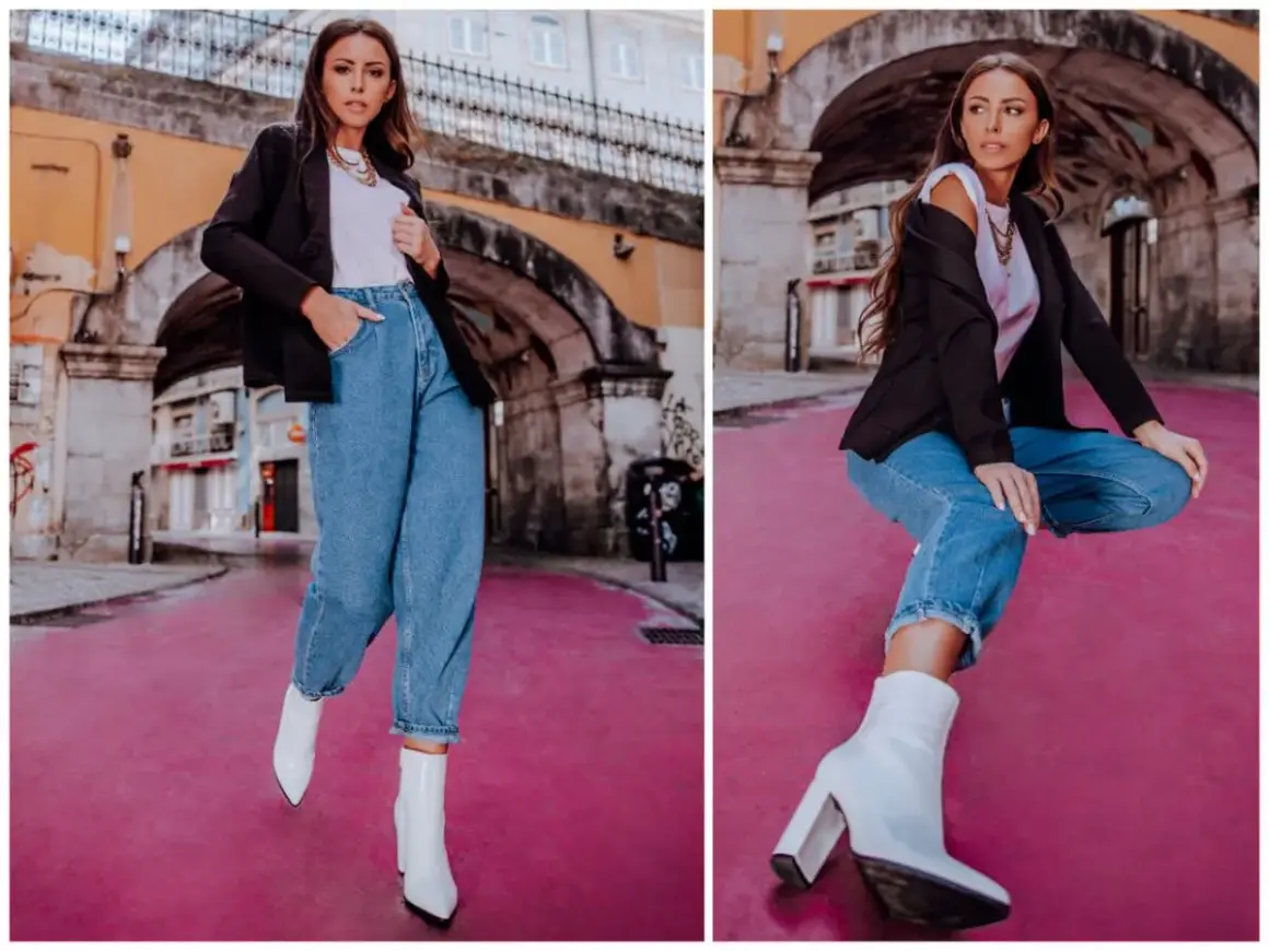 Kobieta w modnych mom jeans stylizacjach, czarnej marynarce i białych kozaczkach na różowym tle.