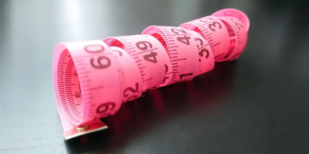 R&oacute;żowa taśma miernicza zwinięta w spirale, z widocznymi numerami. Może posłużyć do mierzenia obwod&oacute;w, ale nie pomoże na za szerokie buty po bokach.