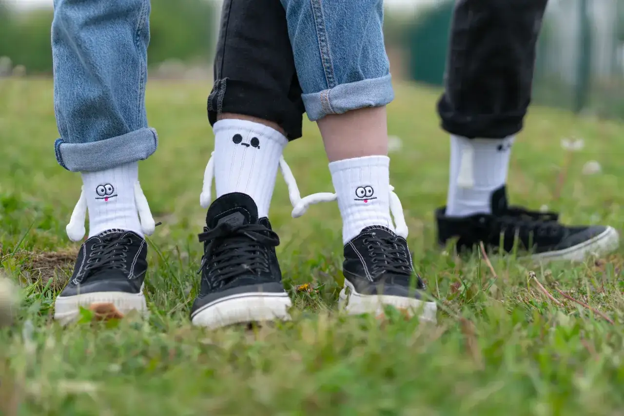 Wysokie skarpetki stylizacje z zabawnymi postaciami i czarne trampki na trawie.